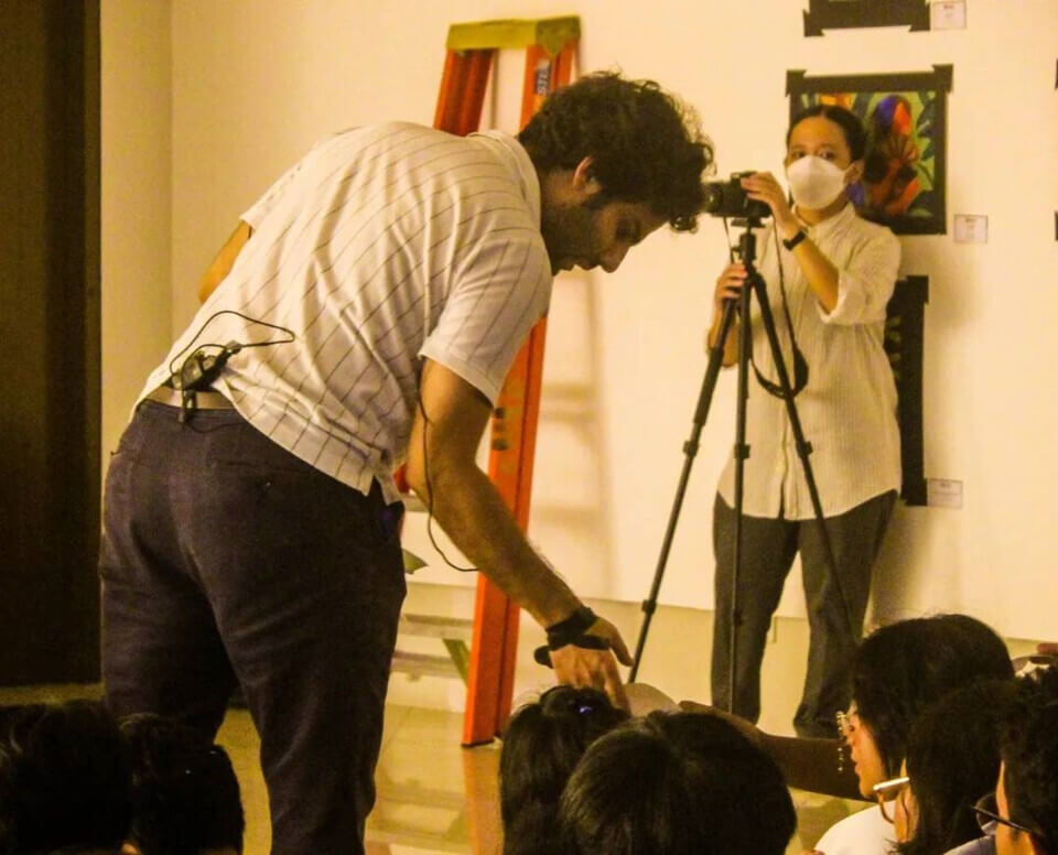 The performer leans forward to take a map fragment from one of the audience members in the first row.
