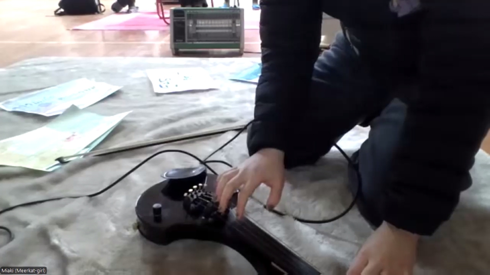 miaki, having placed the Cantini on a mat, plucks its strings.