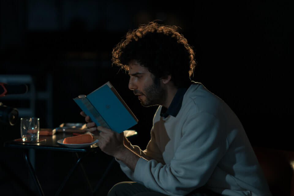 The performer sits, further from the table  and reads a book