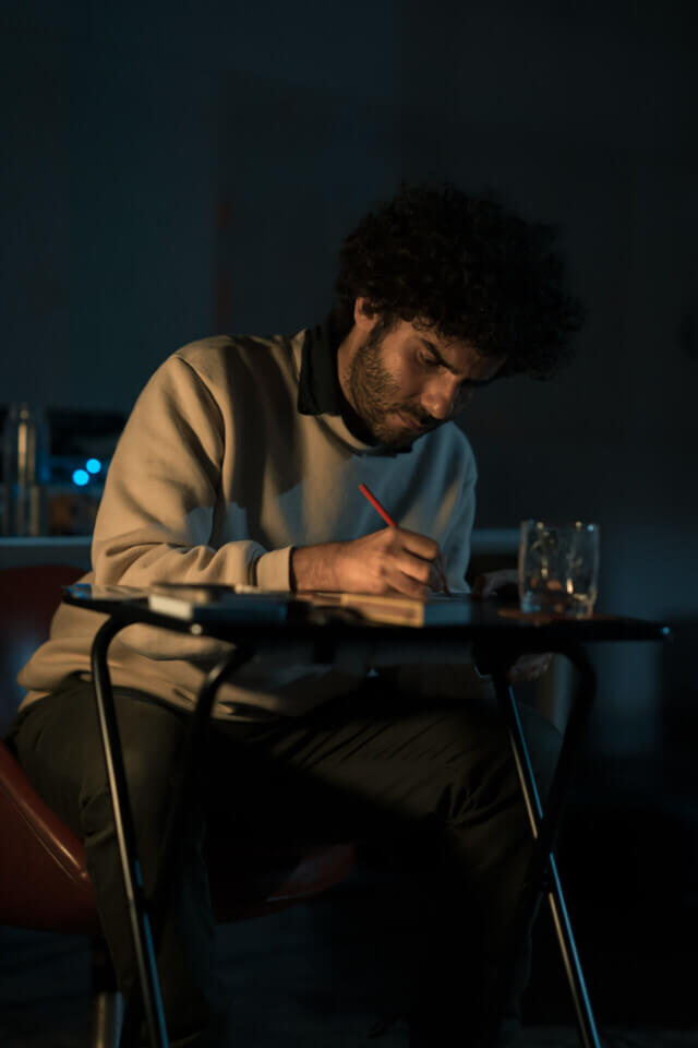 Lit from a side lampt, the performer sits at the desk and writes with a pencil