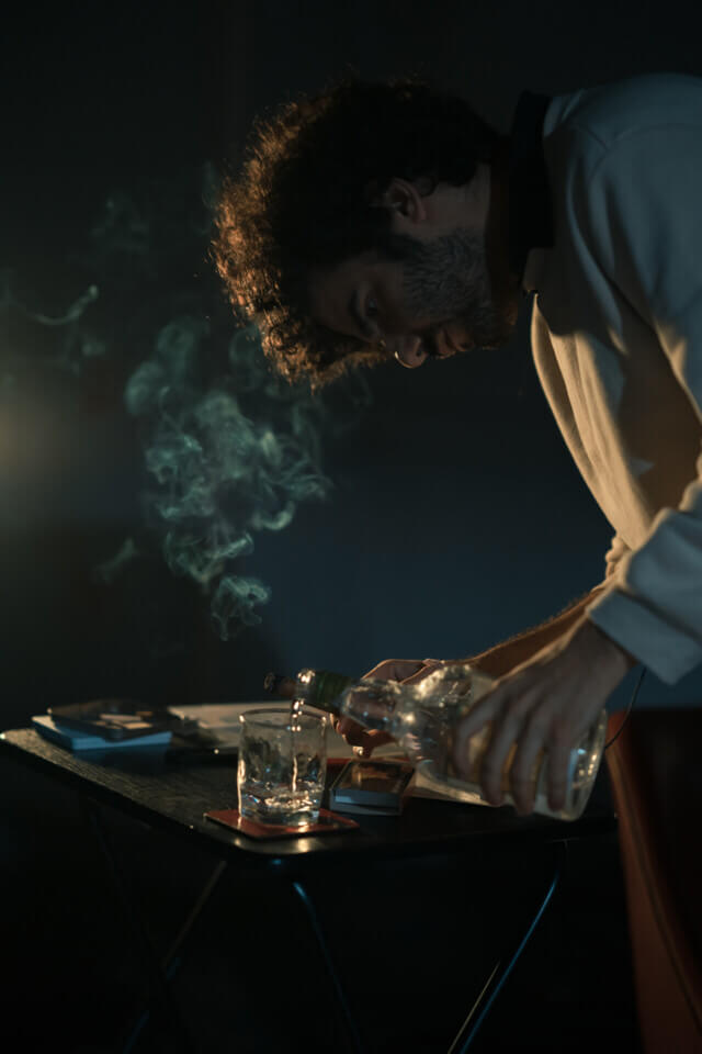 Smoke from the lit cigar ascends as the performer leans over to pour rum into the glass.