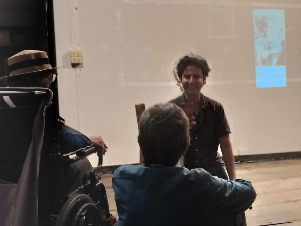 The performer smiles and takes a photo of Chumpon, an older man, seated next to the wheelchair of his wife.