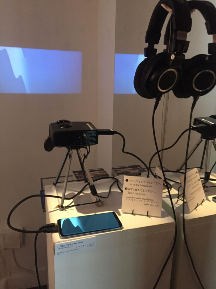 an android device running '...like tears in rain sits on a pedestal with an info card, headphones and a projector. The projector duplicates the image on to the wall.