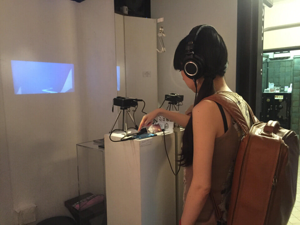 a woman wearing the headphones, touches the android with one hand. Curves appear on the wall projection