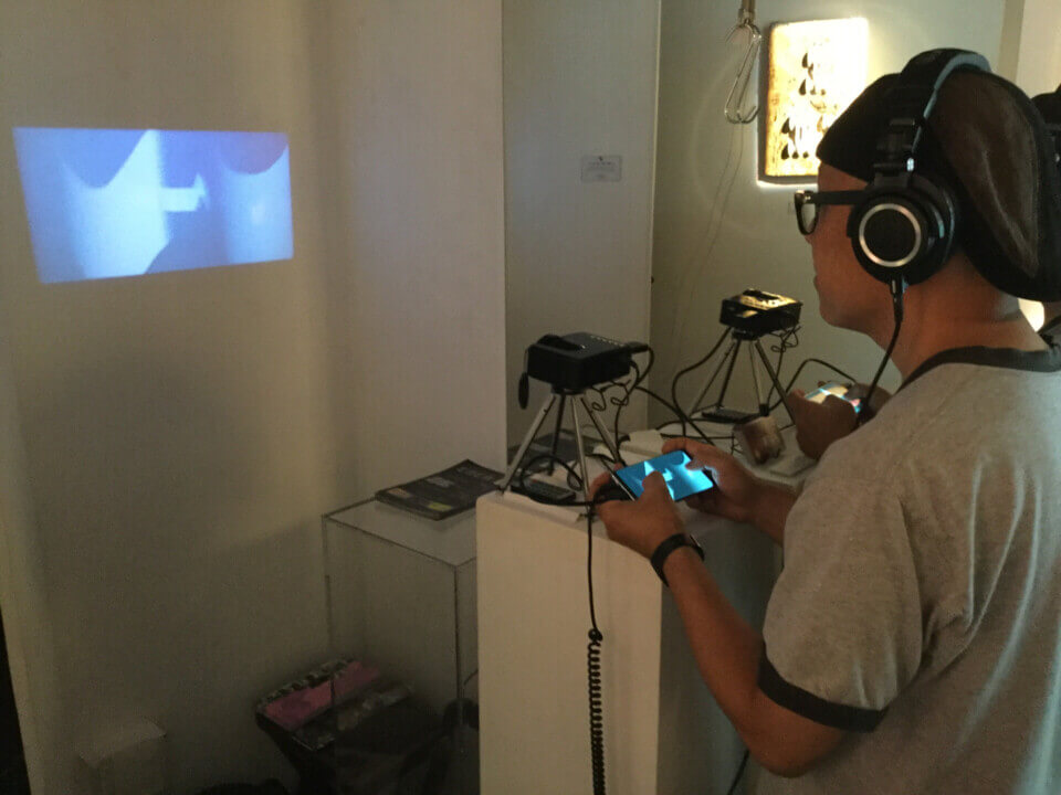 Tsutsumi Yoshihiko, owner of Y's Arts, wears the headphones, holds the android device in both hands and looks at the curves in the projection