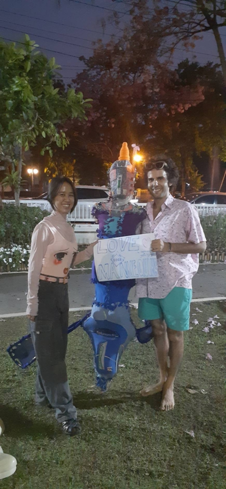 juno and stephan stand smiling with the blue mannequin and the game sign between them.