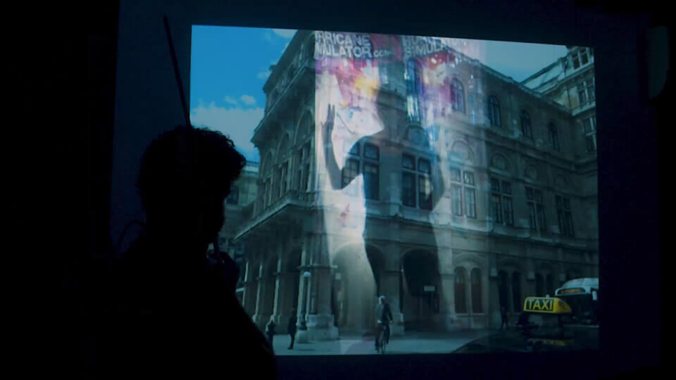 sillhouette of the performer, playing MIDI violin in front of a projection. The projection shows a composite of two images. One of a woman in Hurricane Simulator. The other of a building in Vienna, perhaps the Staatsoper.