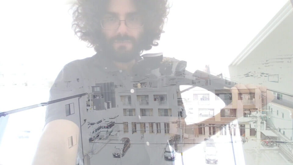 vertical split-screen. the top half shows a bespectacled Koujiro looking to the side. The bottom half is a composite of stephan in his apartment and an outside camera showing the space between two apartment buildings