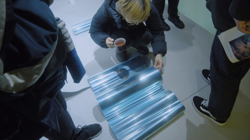an event guest holding a teacup crouches to look into a sheet of mirror foil