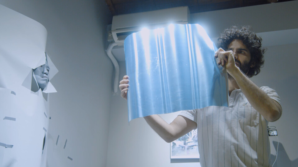 the performer holds a half sheet of mirror paper in front of him, which reflects light brightly