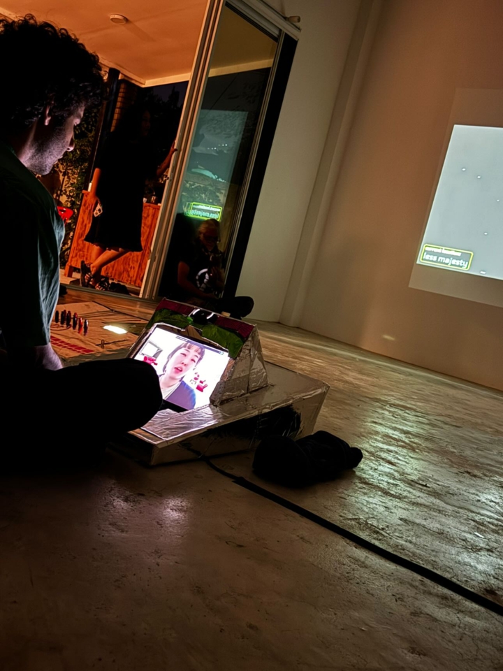 the artist looks down at the console, which shows the face of miaki. They are having a video-call