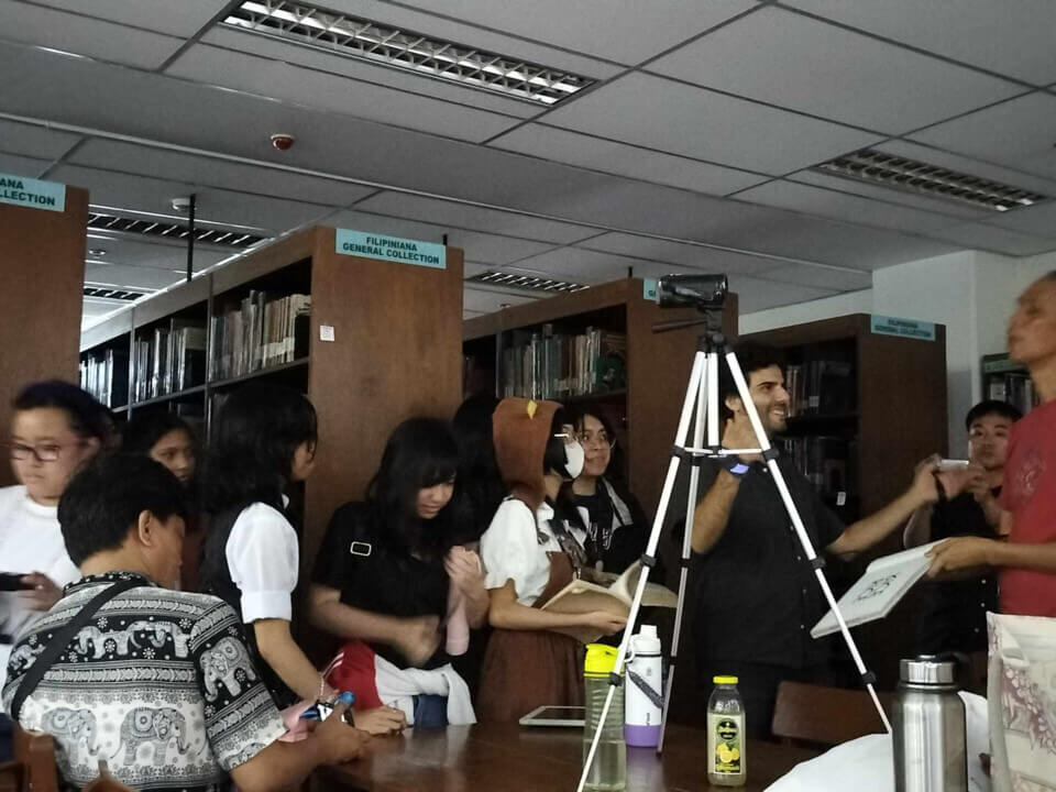 The performer laughs with a man holding a book for him. Students are lined up holding books
