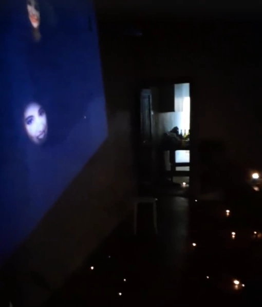 the living room on day 3 of the event. faces can be seen floating on the left wall while many candles are strewn about on the floor and tables