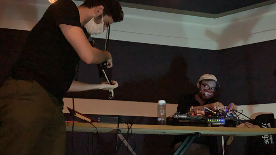 stephan e perez plays midi violin while eric beyeler sits at a table manipulating effect pedals